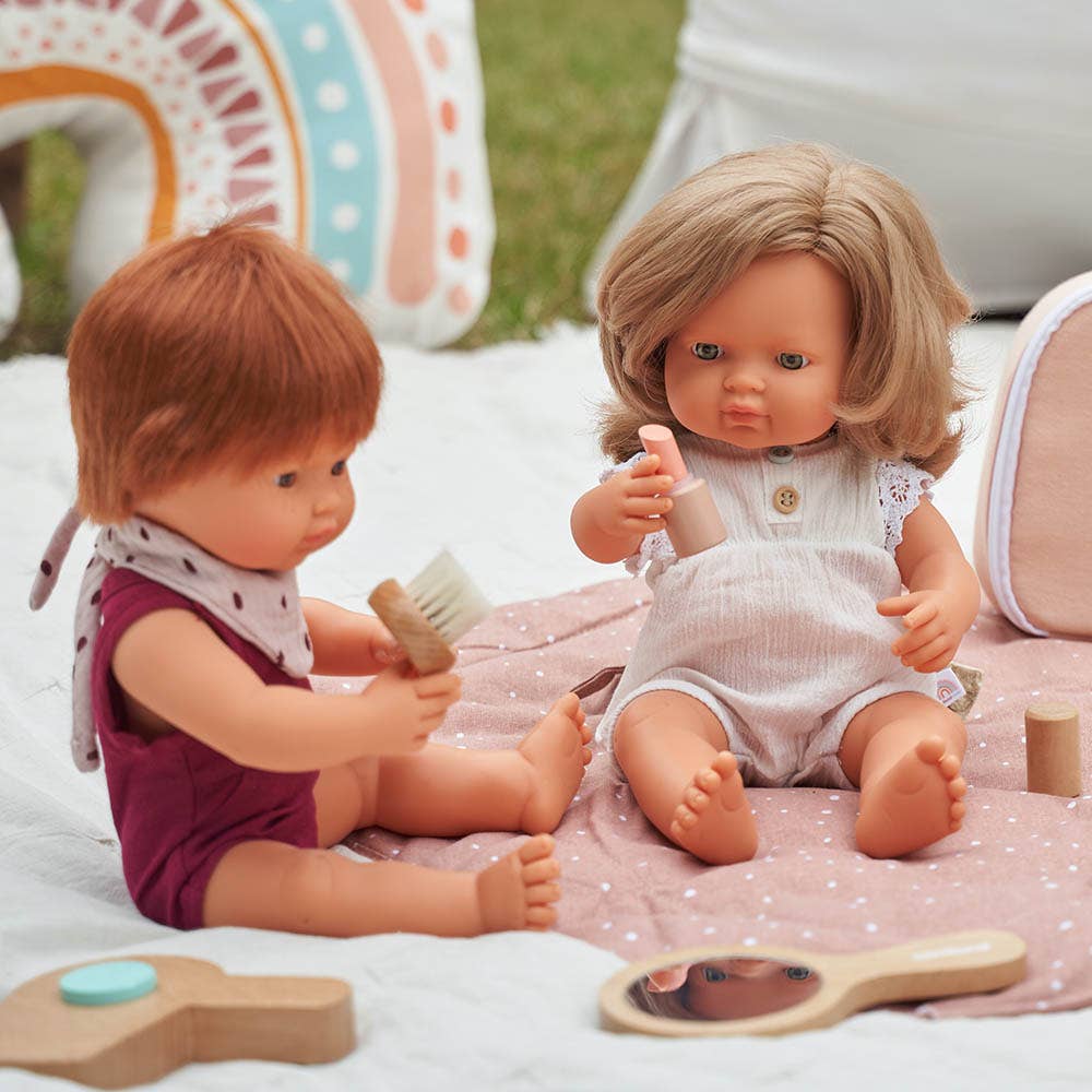 Two dolls playing with toys on a blanket outdoors