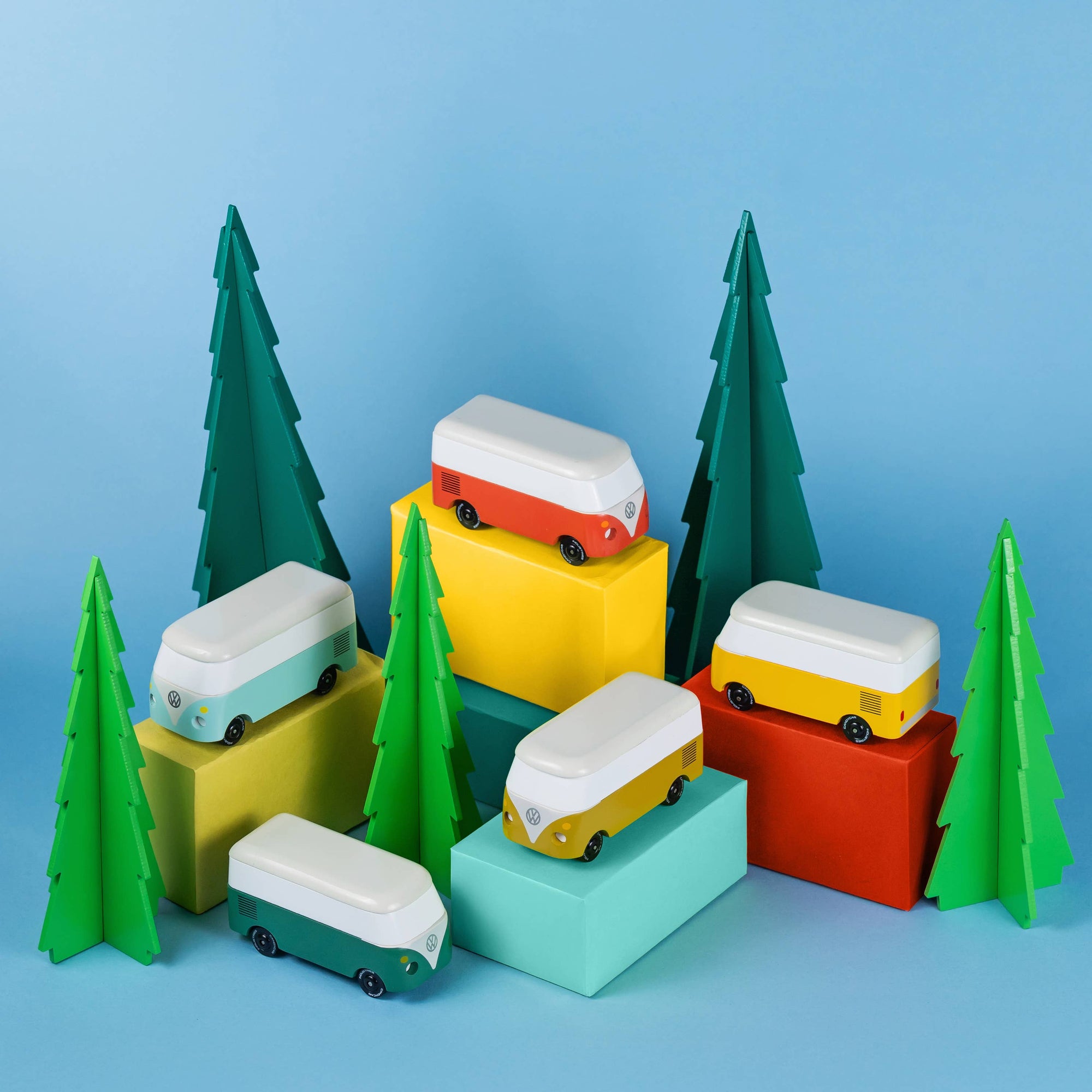Colorful toy vans on geometric blocks with green trees against a blue background