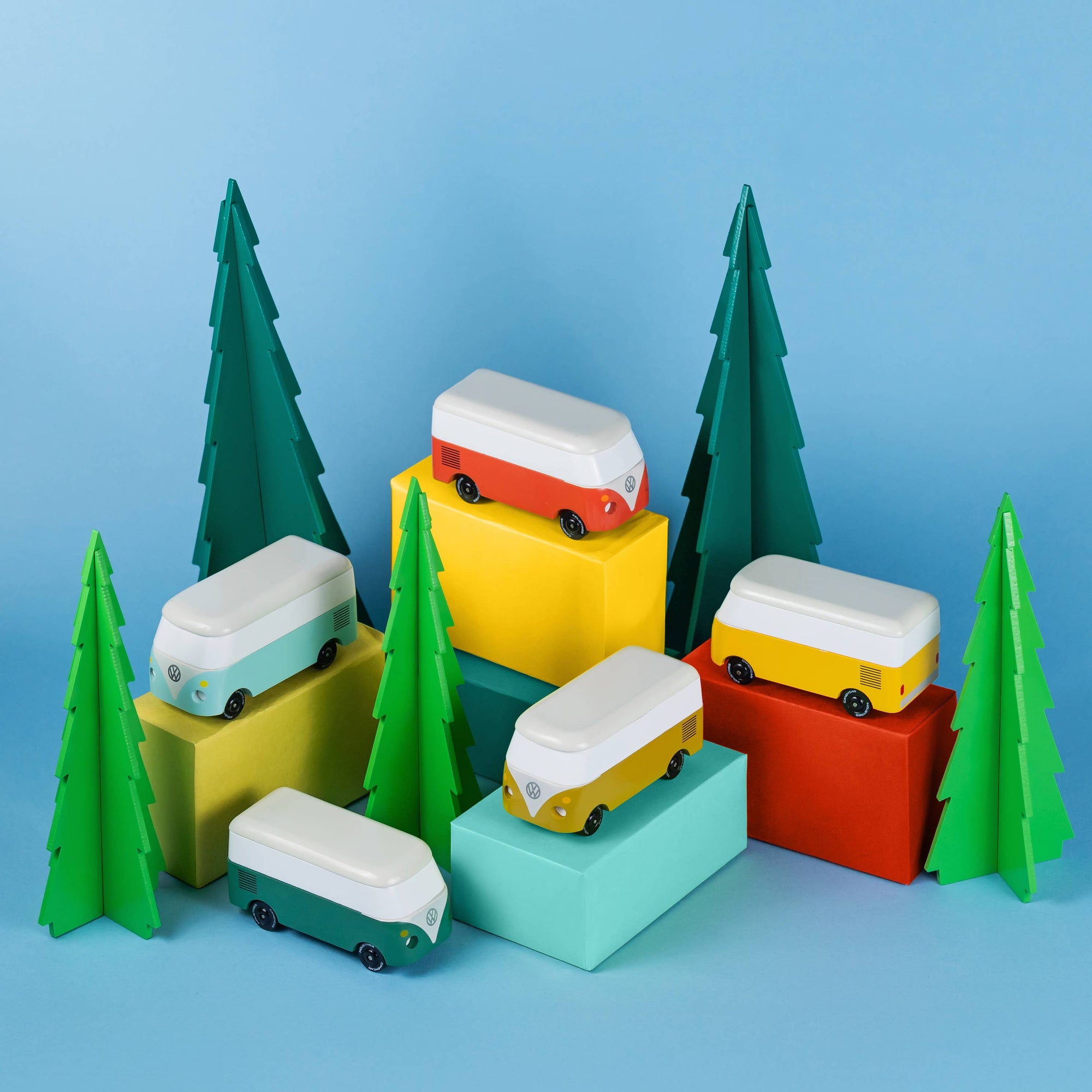 Colorful toy vans on geometric blocks with green trees against a blue background
