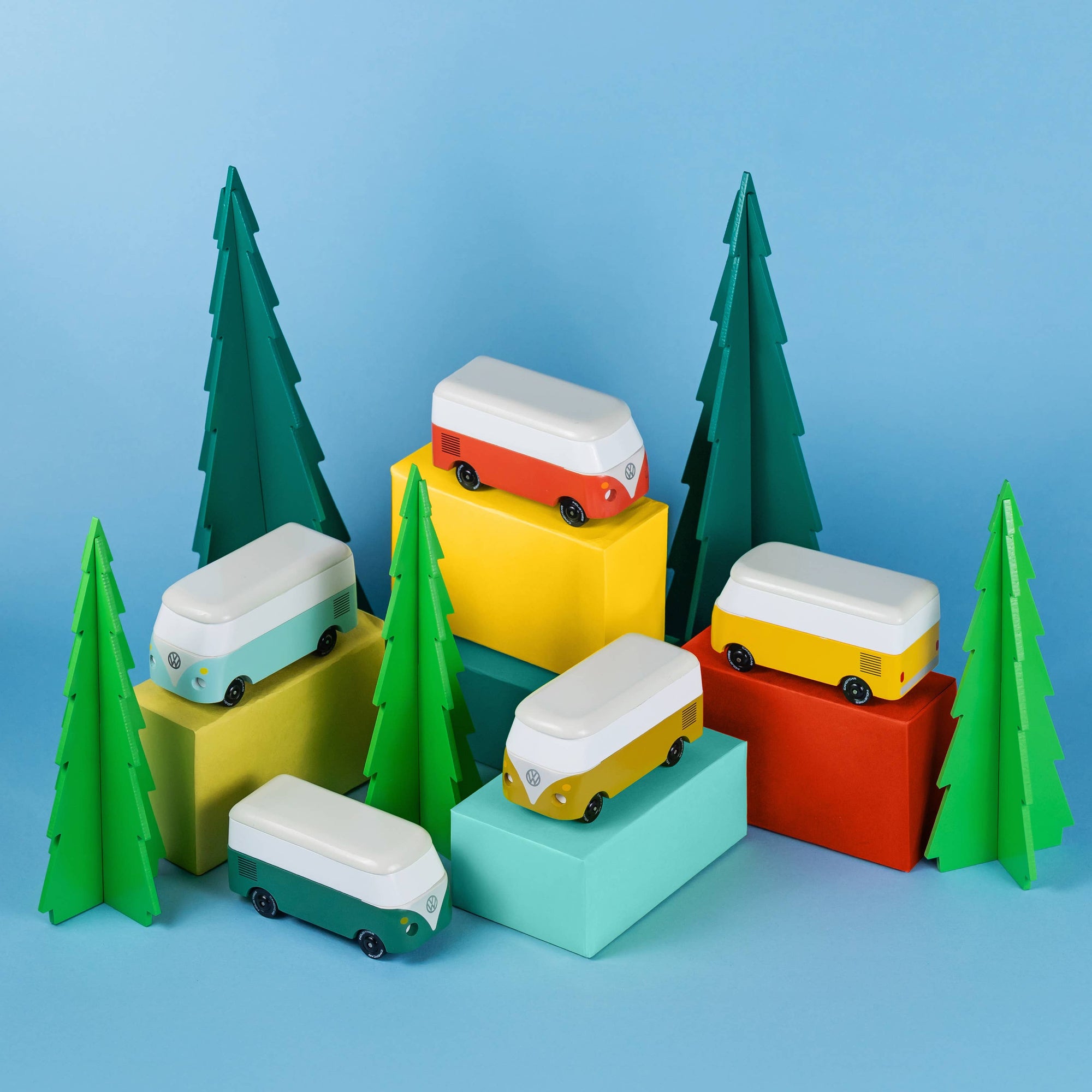 Colorful toy vans on geometric blocks with green trees against a blue background