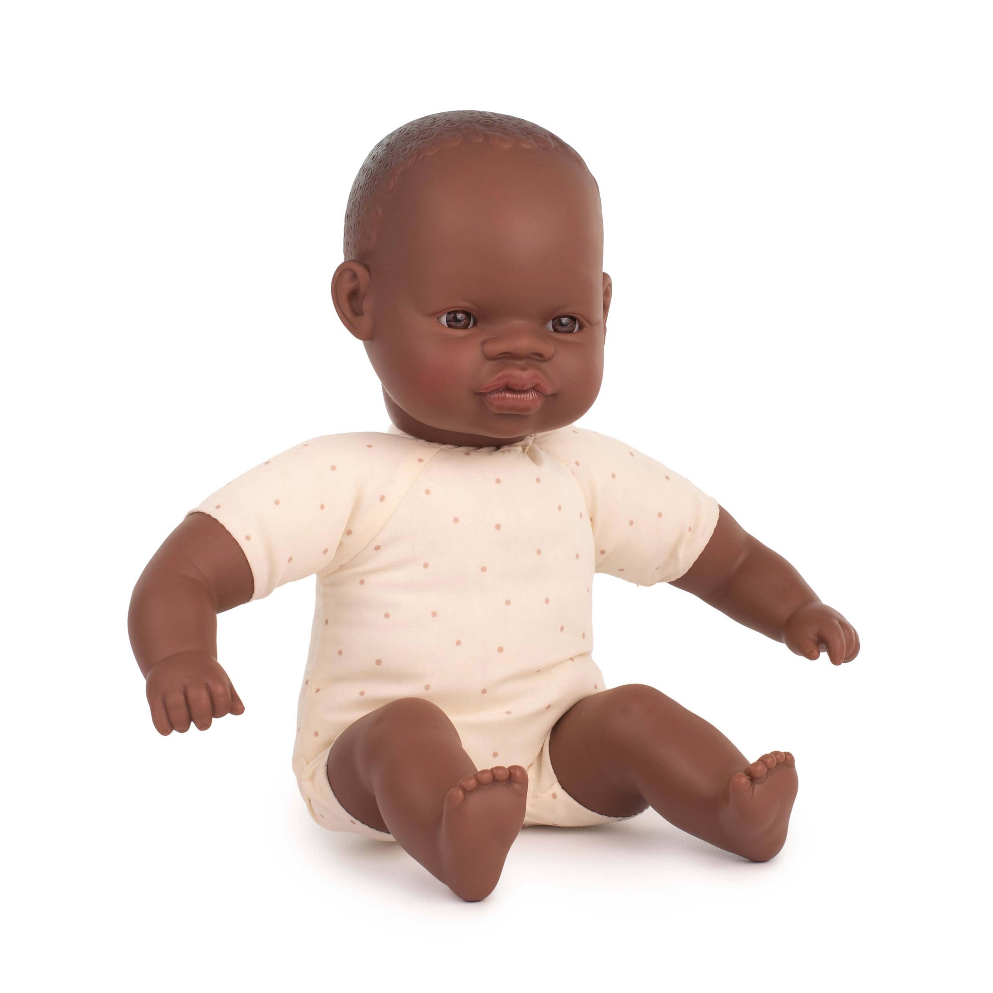 Baby doll with brown skin and dark hair wearing a white onesie on a white background