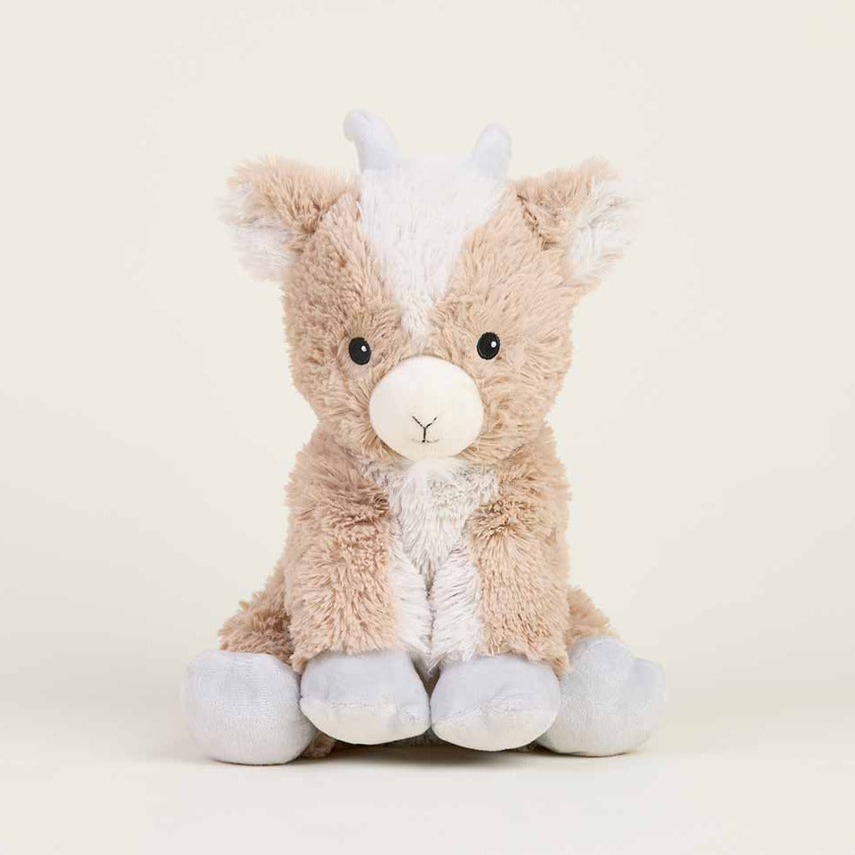 A plush stuffed animal shaped like a cow, made of soft tan and white faux fur, sitting against a plain light beige background.