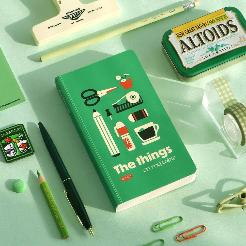 Green notebook with illustrations and text on a light green background with stationery items.
