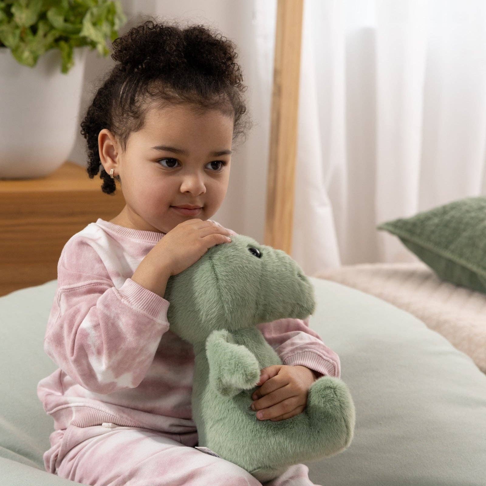 Child holding a green plush toy on a light-colored couch