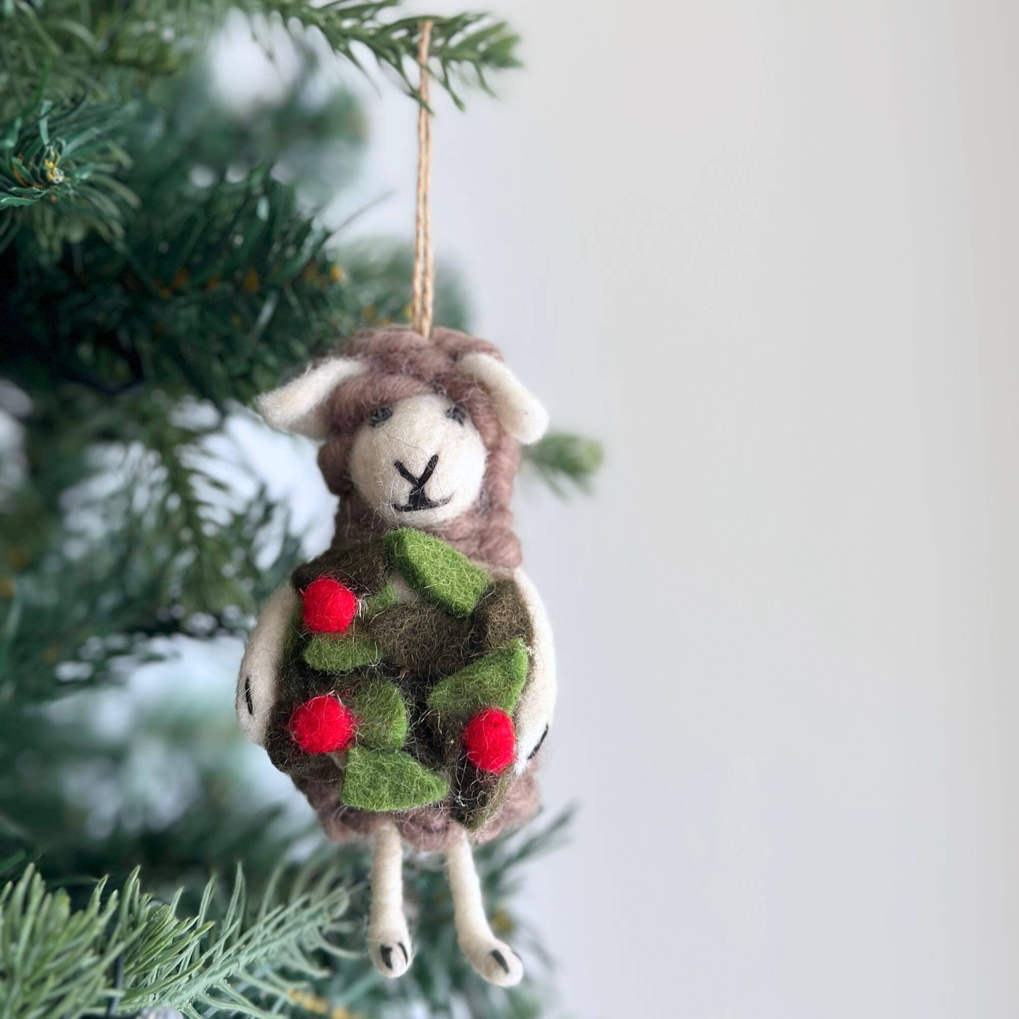 Felted sheep ornament wearing a Christmas sweater with red berries on a tree branch.