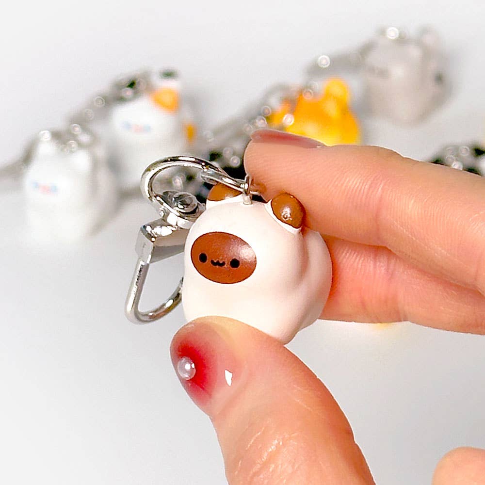 Small white dog-shaped keychain with a brown nose held by a hand against a light background