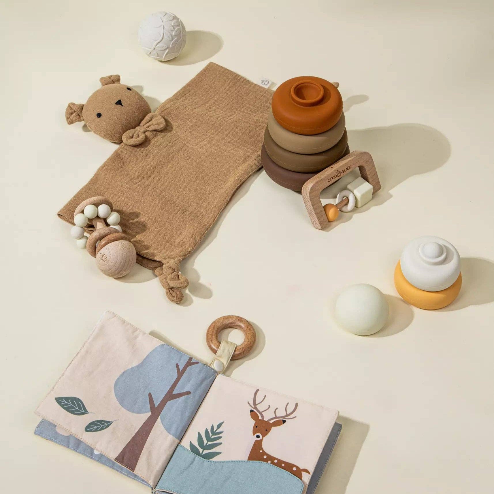 Collection of baby toys including a soft book, rattle, and teether on a neutral background