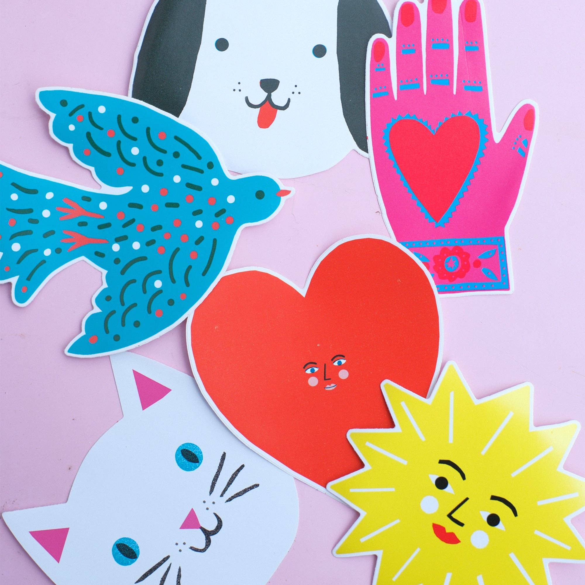 Colorful paper cutouts of a dog, bird, heart, cat, and sun on a pink background