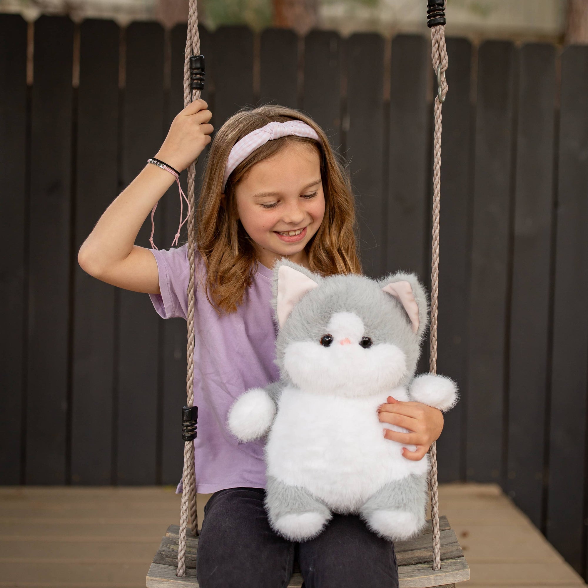 Child on a swing holding a plush toy in a backyard setting