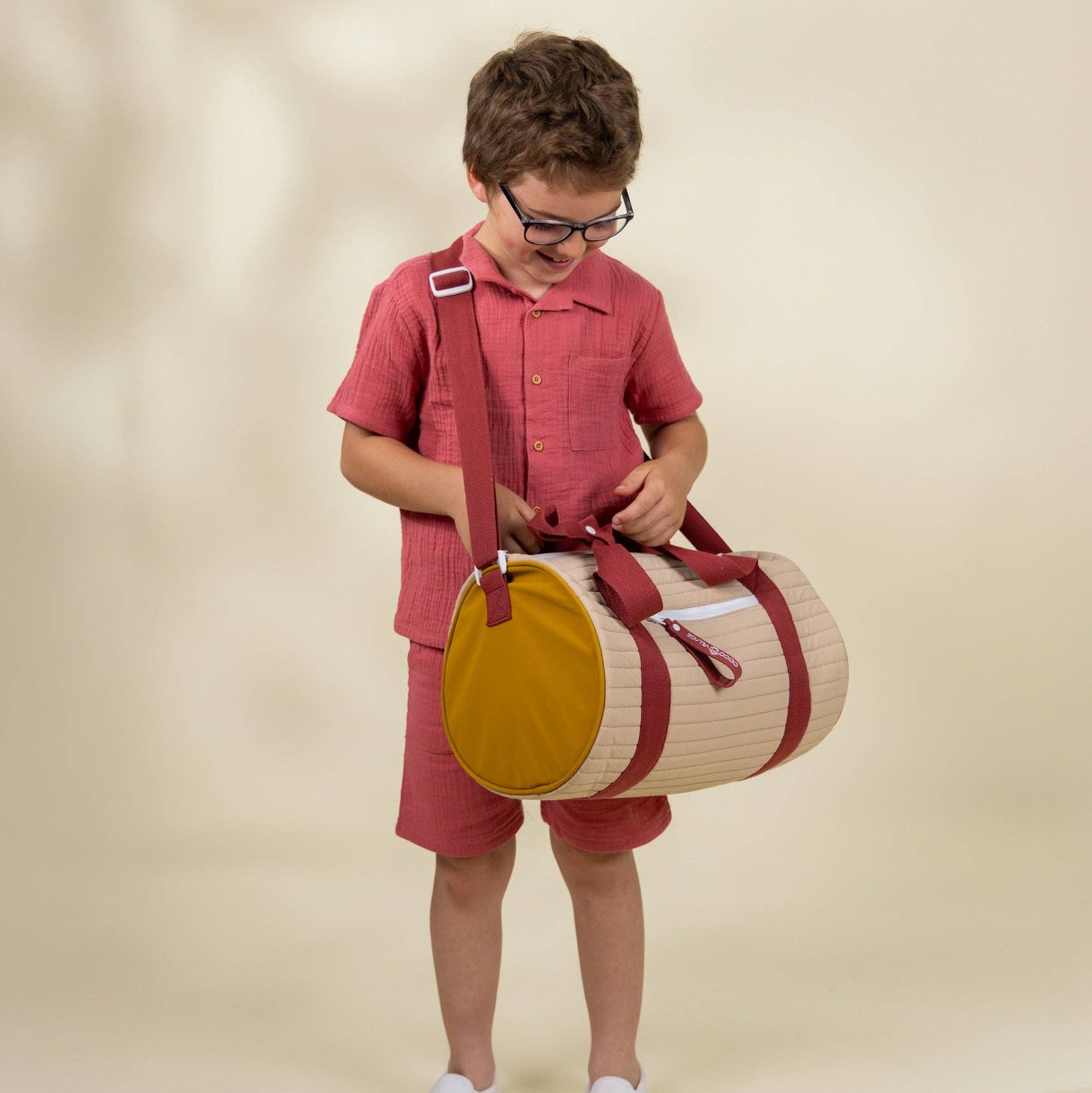 Child holding a round bag with a strap against a beige background