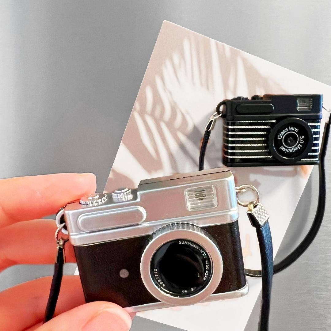 Vintage-style camera held by a hand with a reflective surface in the background