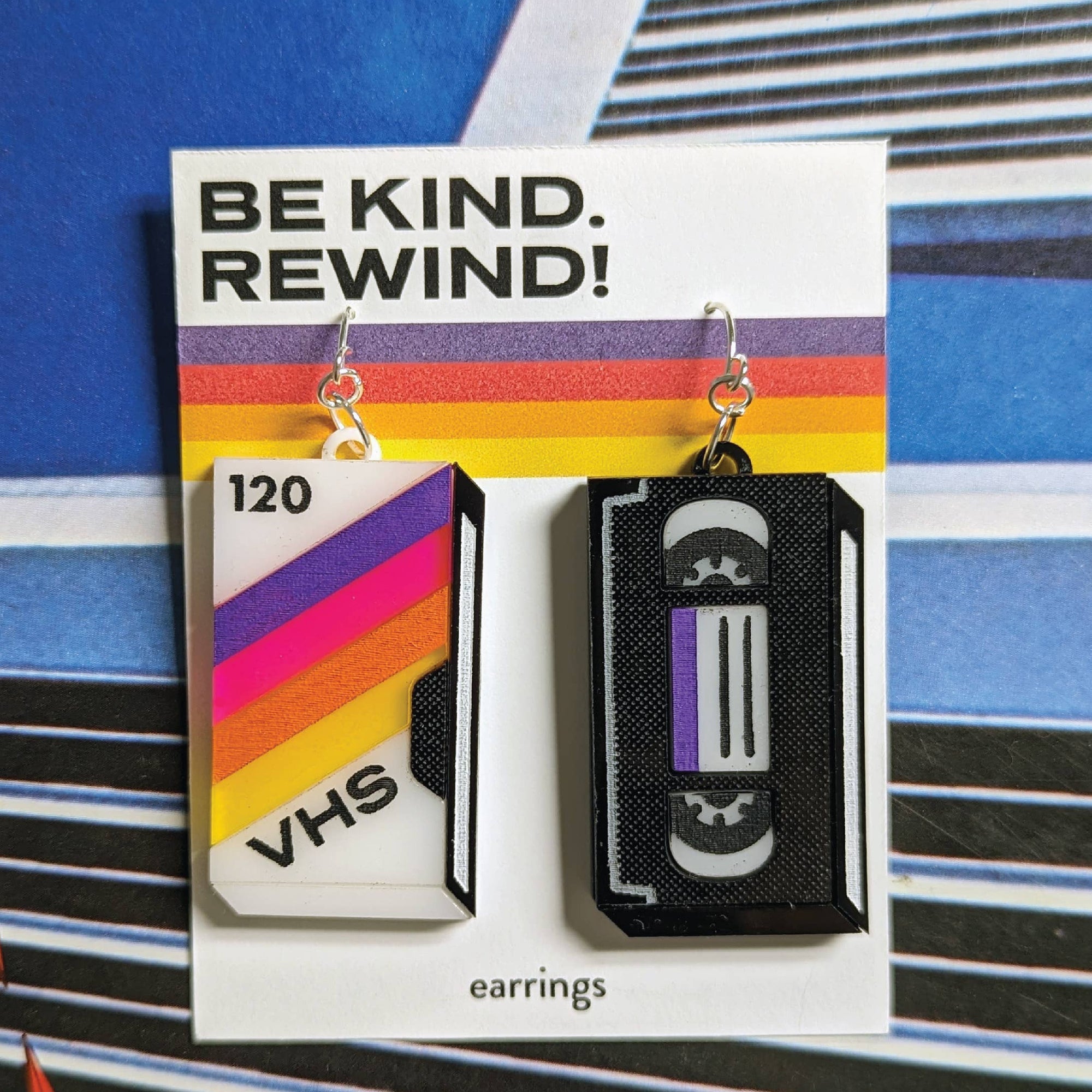 VHS tape earrings on a card with 'Be Kind. Rewind!' text against a colorful striped background.