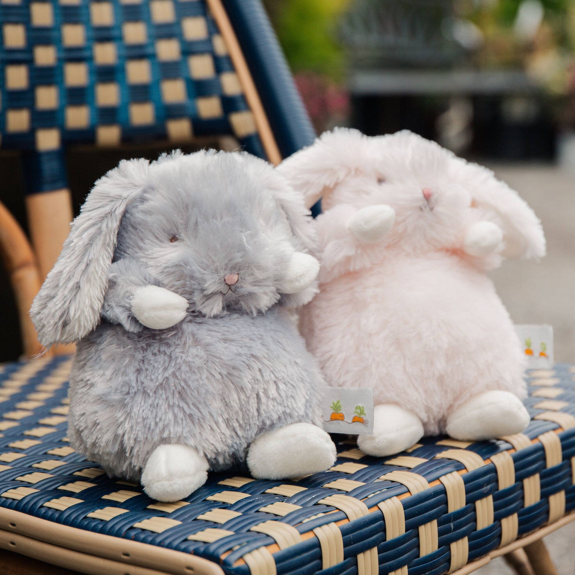Two plush bunny toys, one gray and one pink, sitting on a wicker chair.