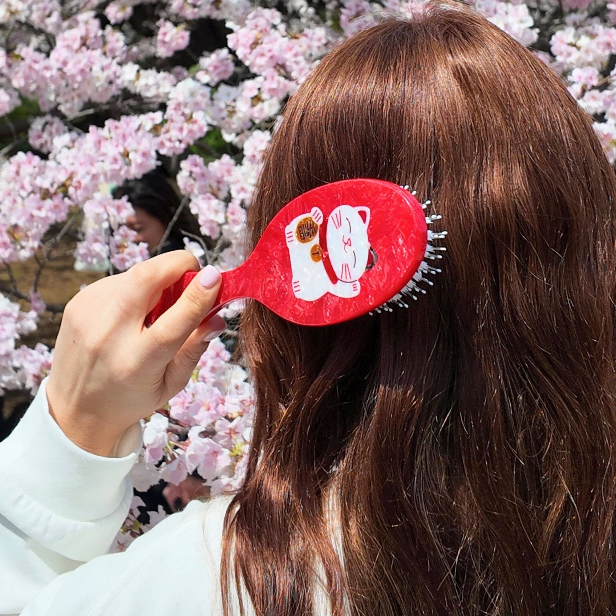 Person using a red hairbrush with a cartoon design against a cherry blossom background