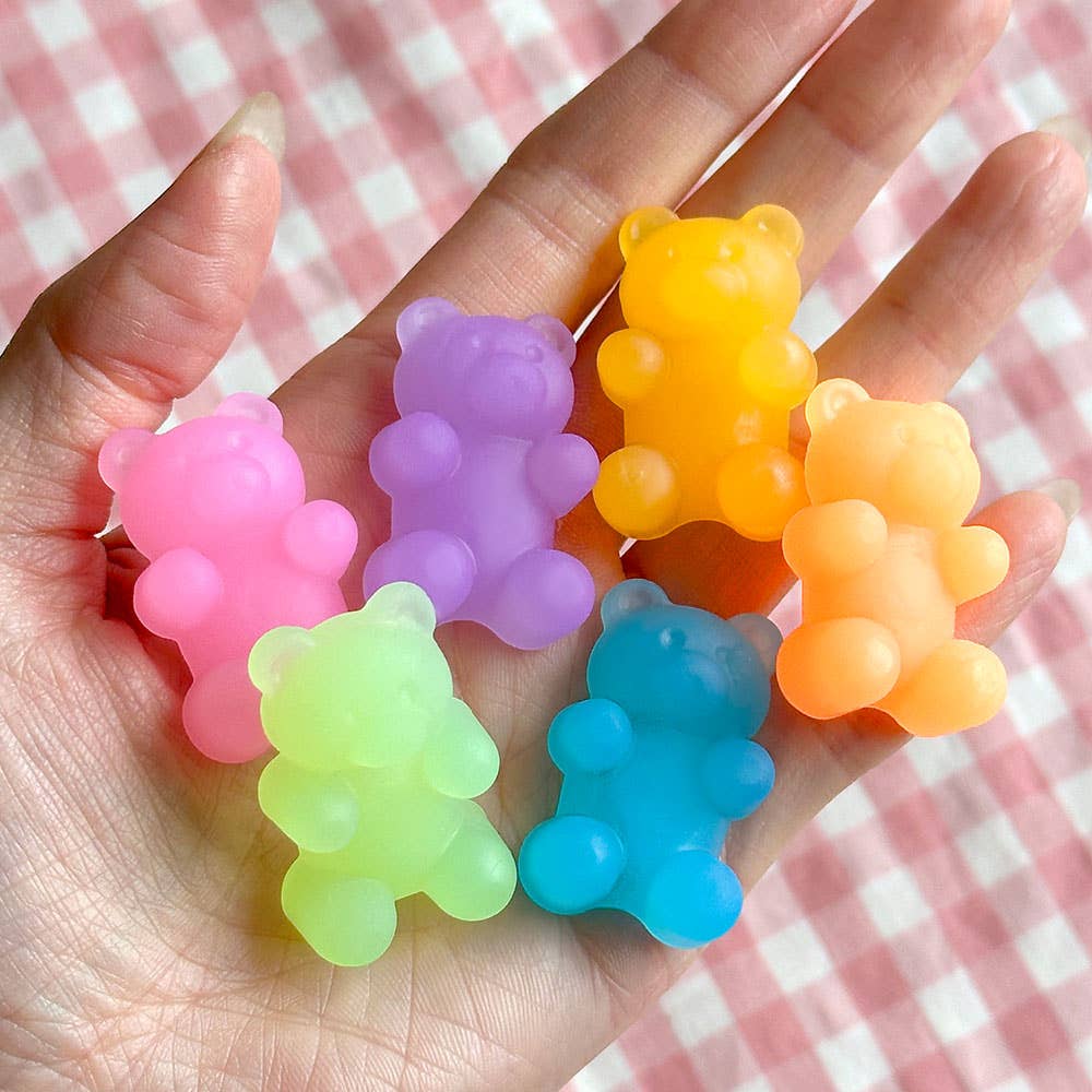 Colorful bear-shaped gummy candies held in a hand with a pink checkered background