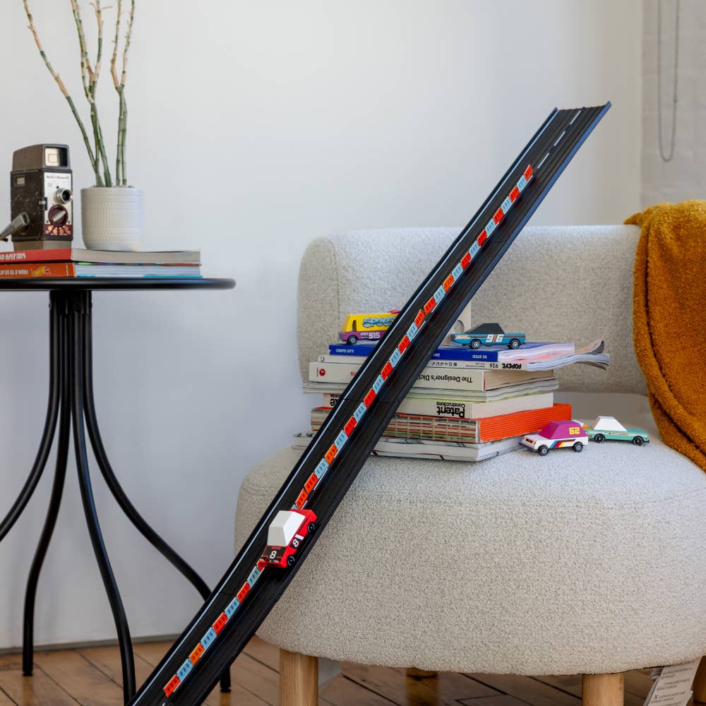 Toy train set on a long track in a living room setting with books and toys.