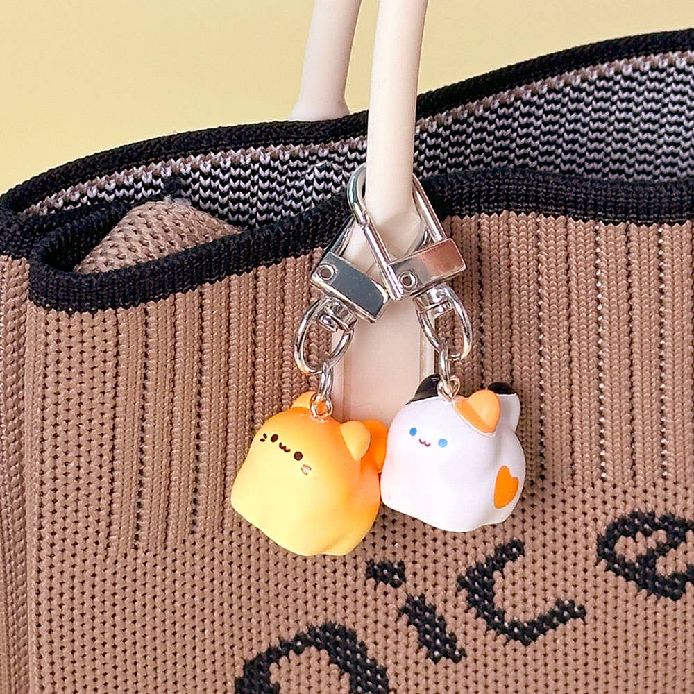 Two small animal-shaped keychains hanging from a bag handle against a beige background.