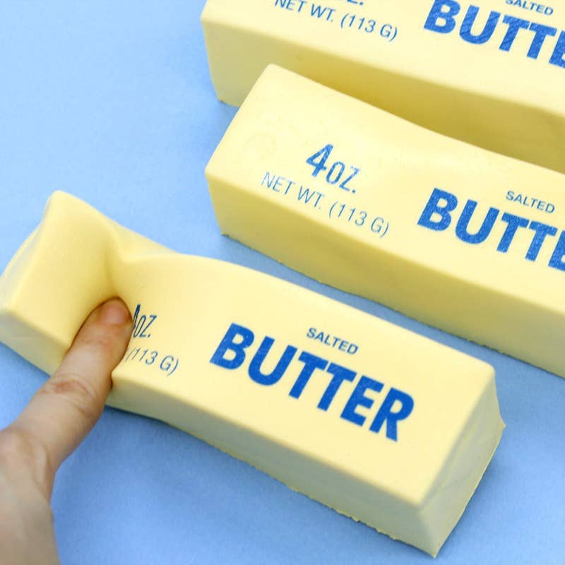 Three bars of salted butter with a hand touching one of them on a blue background