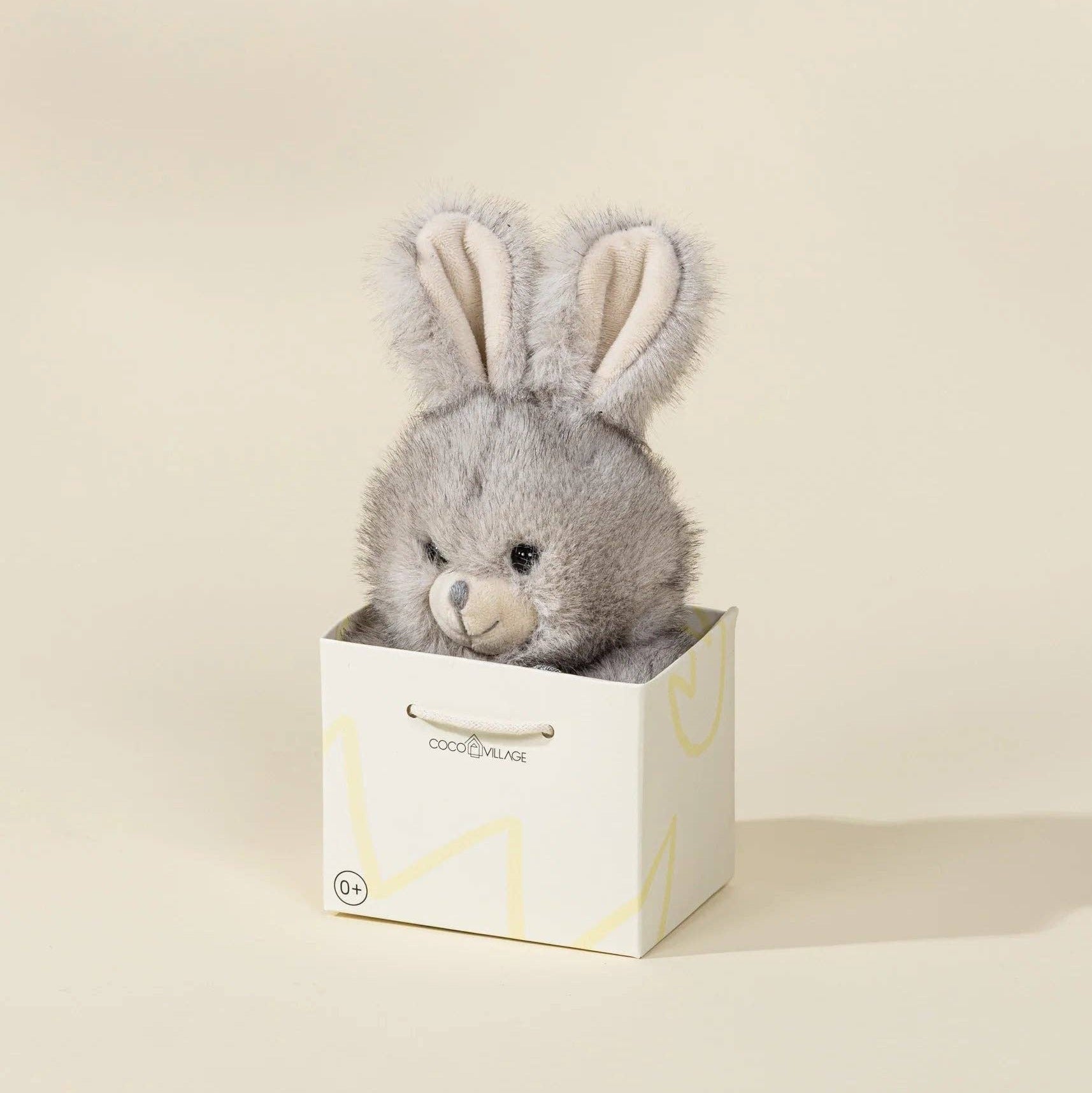 Gray plush bunny toy in a white box on a beige background