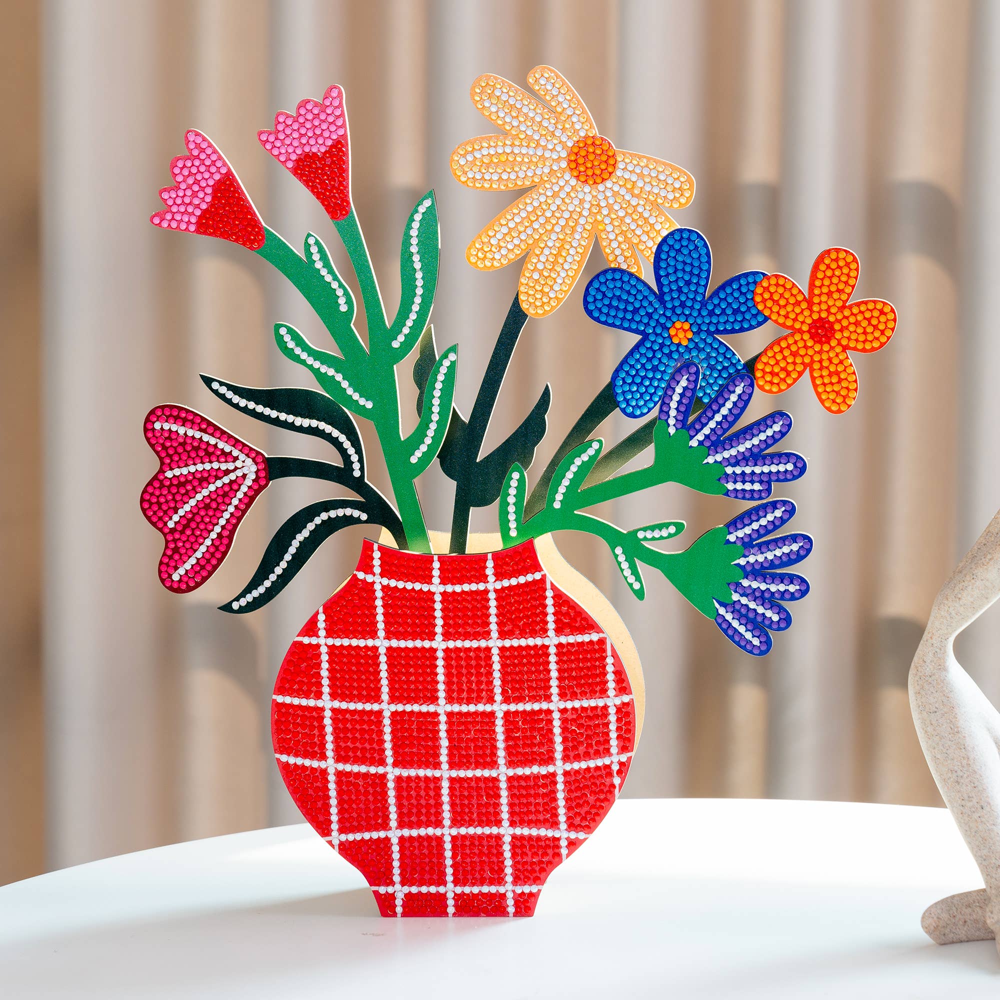 Colorful floral arrangement in a red checkered vase on a white surface with a blurred background