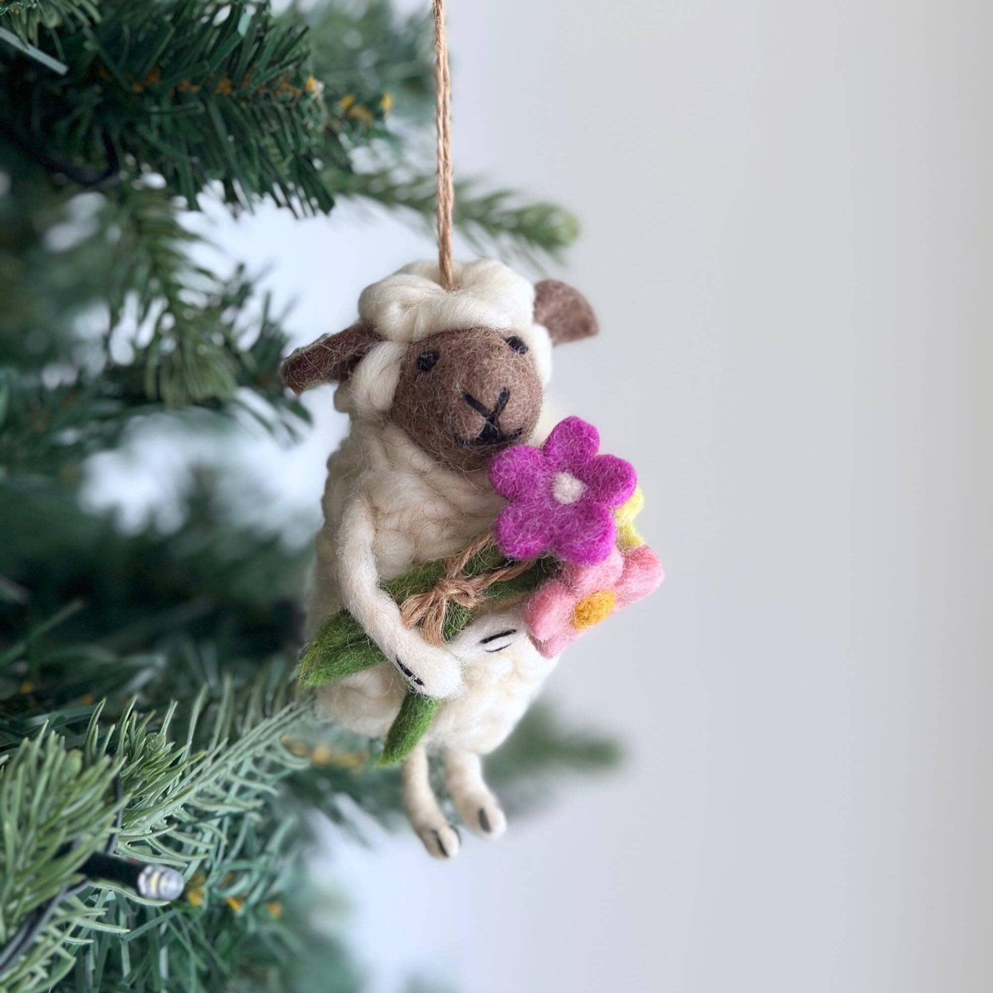 Felted sheep ornament with flowers hanging on a Christmas tree.