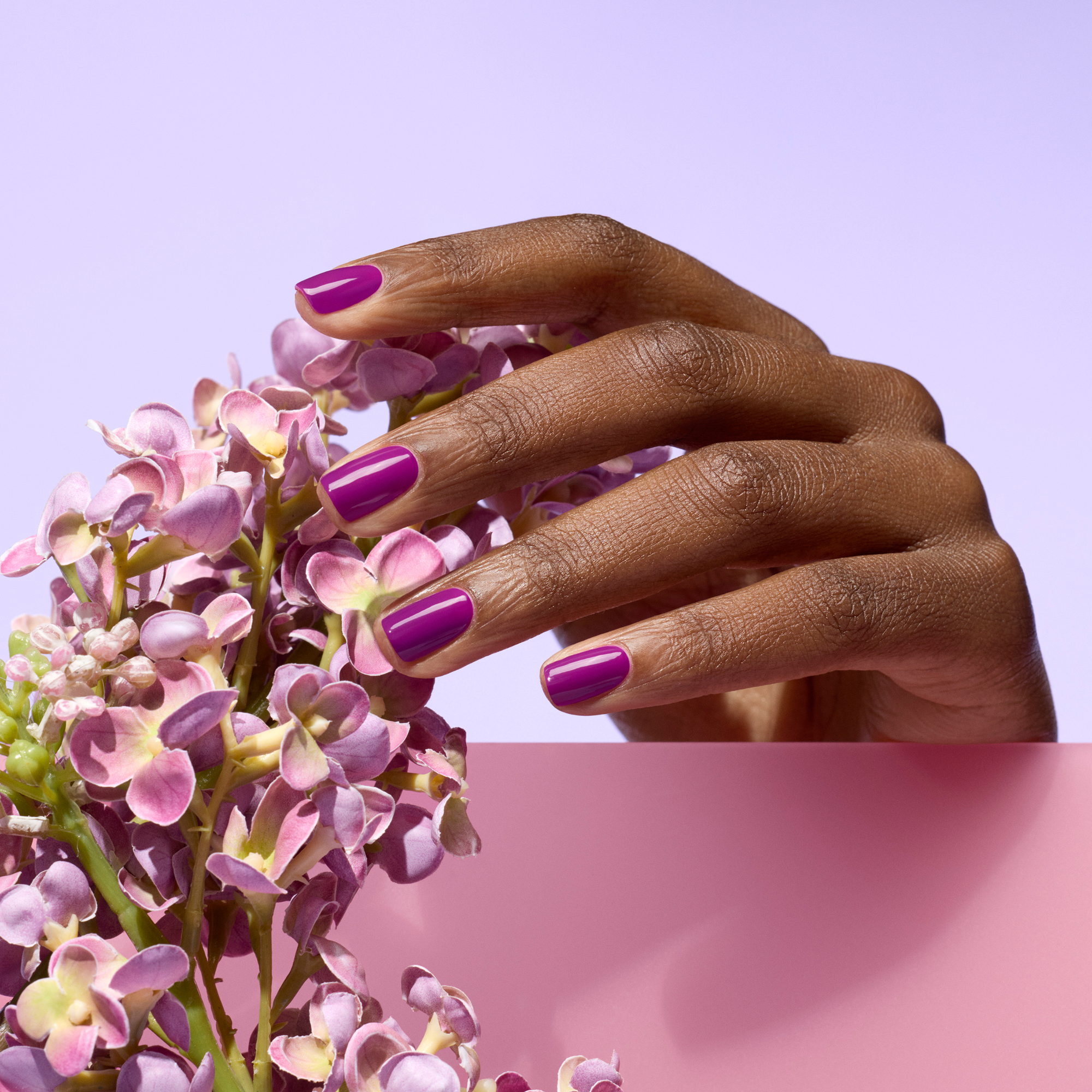 Hand with purple nail polish holding a bouquet of pink flowers against a light purple background