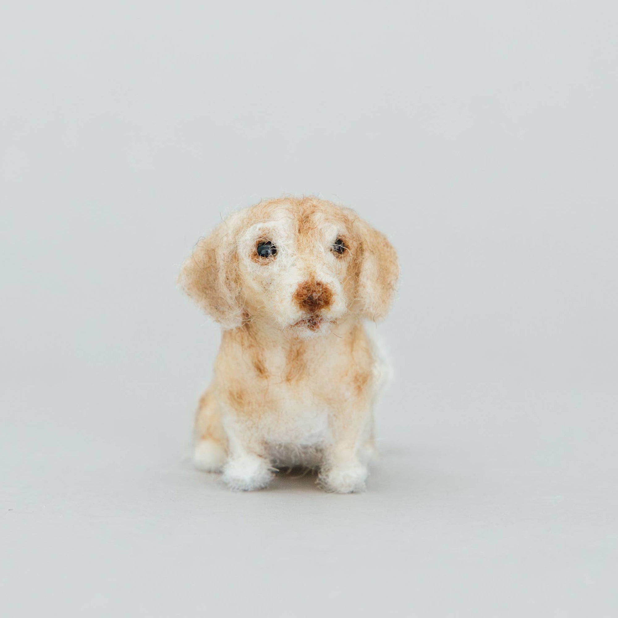 A small realistic dog figurine or miniature puppy sitting upright against a plain light gray studio background.