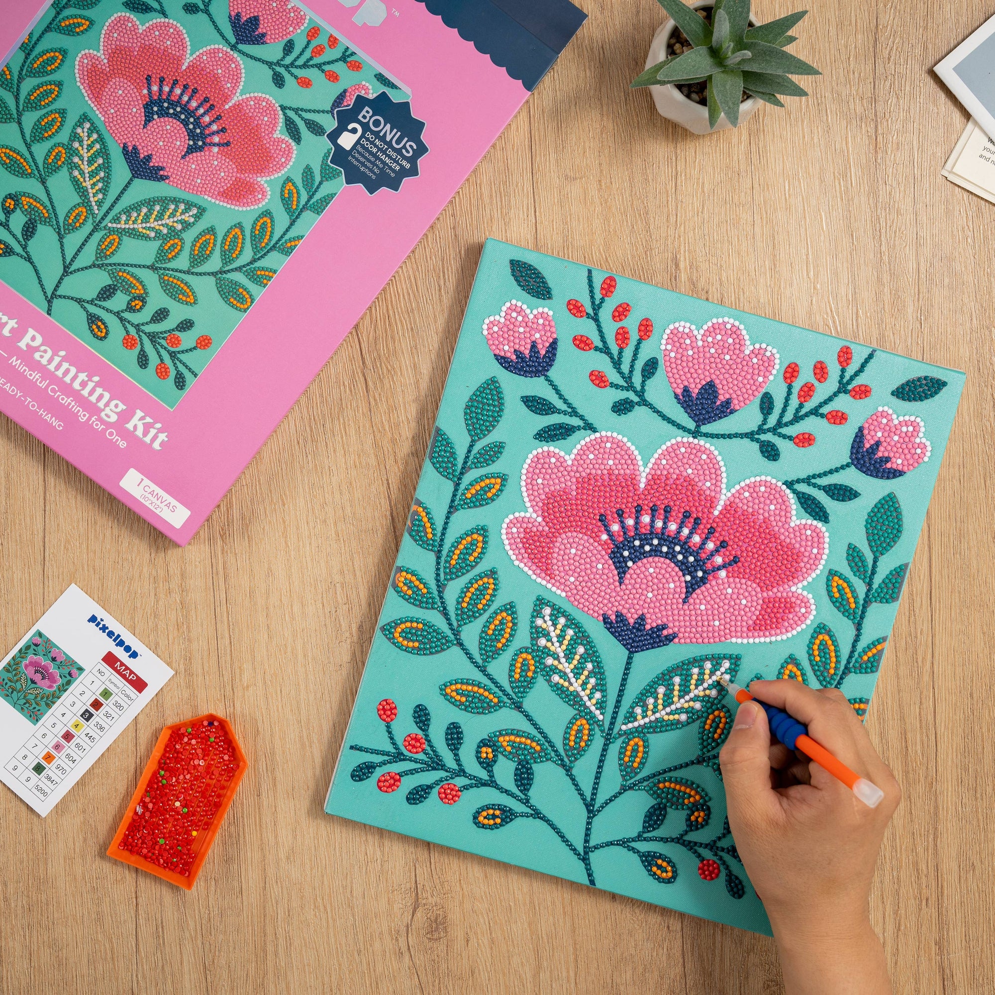 Floral diamond art painting kit being worked on with a pen on a wooden surface.