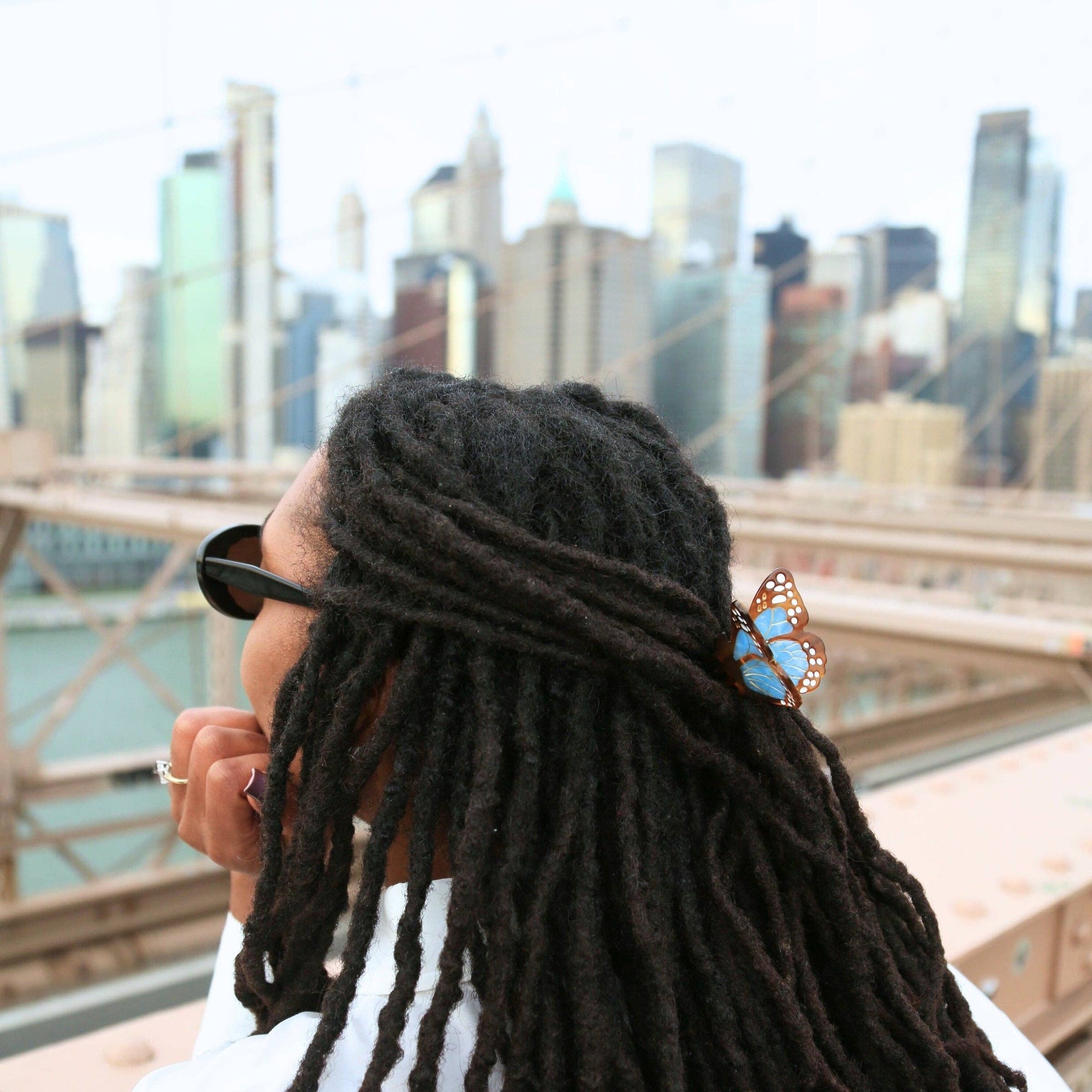 Person with long dreadlocks sitting on a bridge with a city skyline in the background