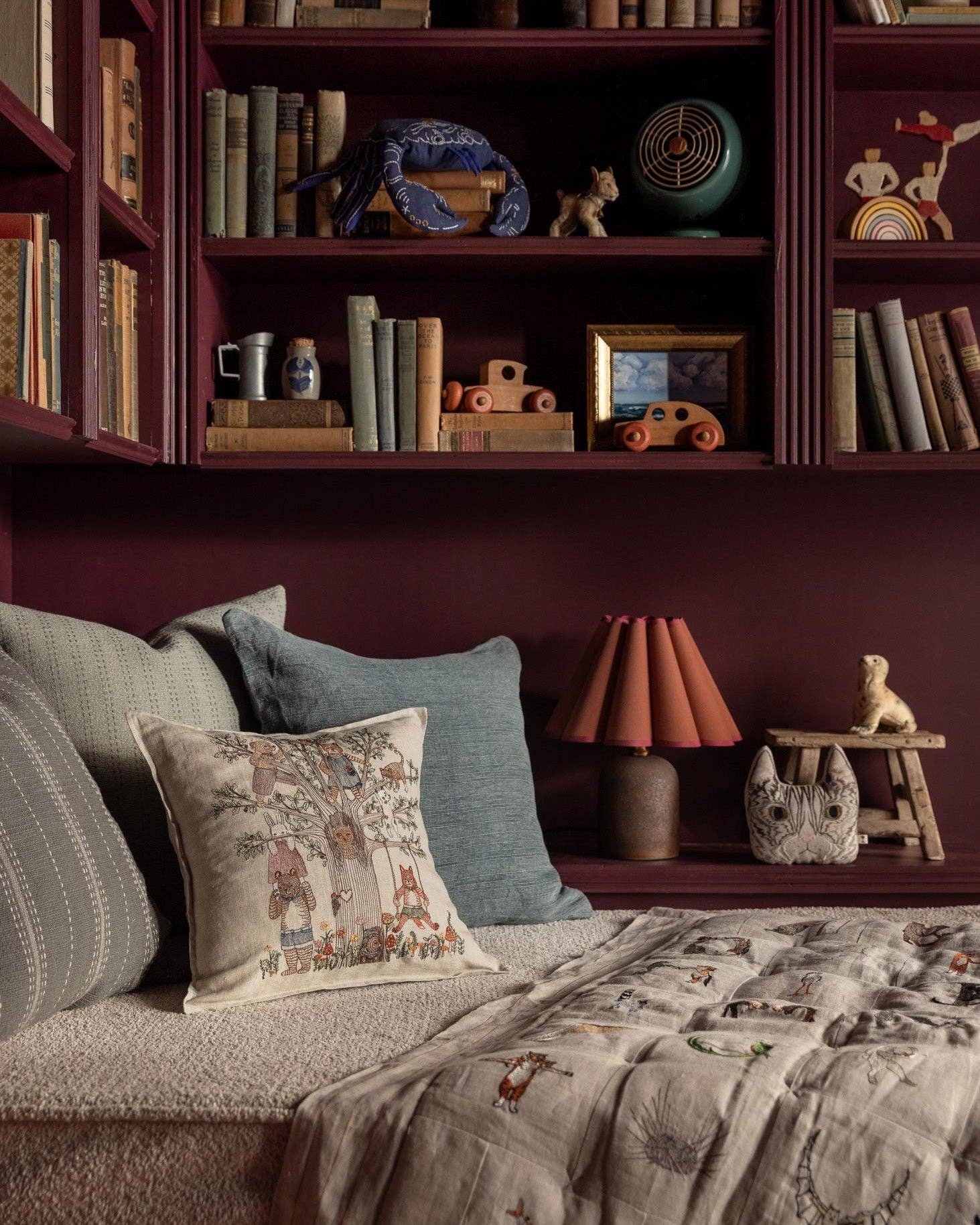 Cozy bedroom with bookshelf, pillows, and lamp.