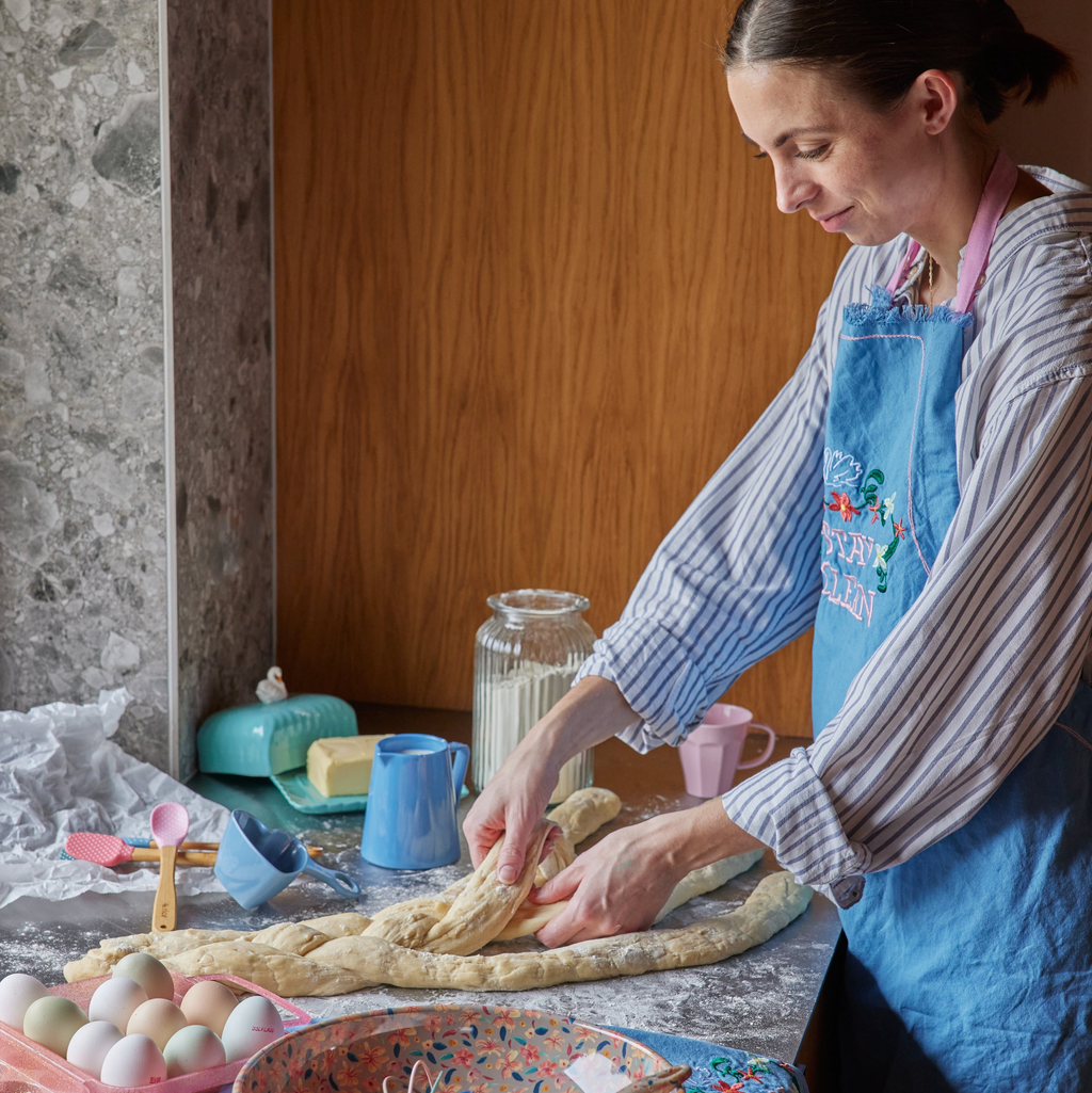 Woman in a kitchen preparing dough, wearing a blue apron.