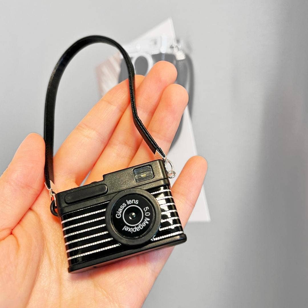 Small camera-shaped keychain held in a hand against a neutral background
