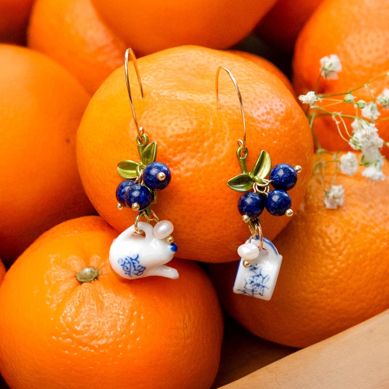 Earrings with ceramic rabbit charms on a pile of oranges