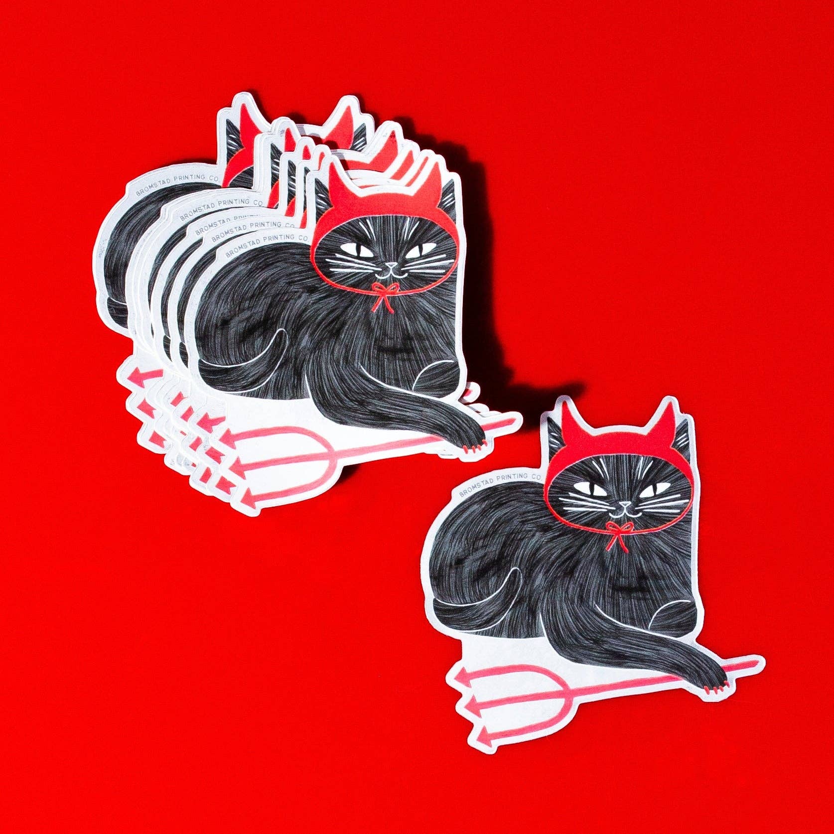 Two black cats with red devil horns and tails on a red background