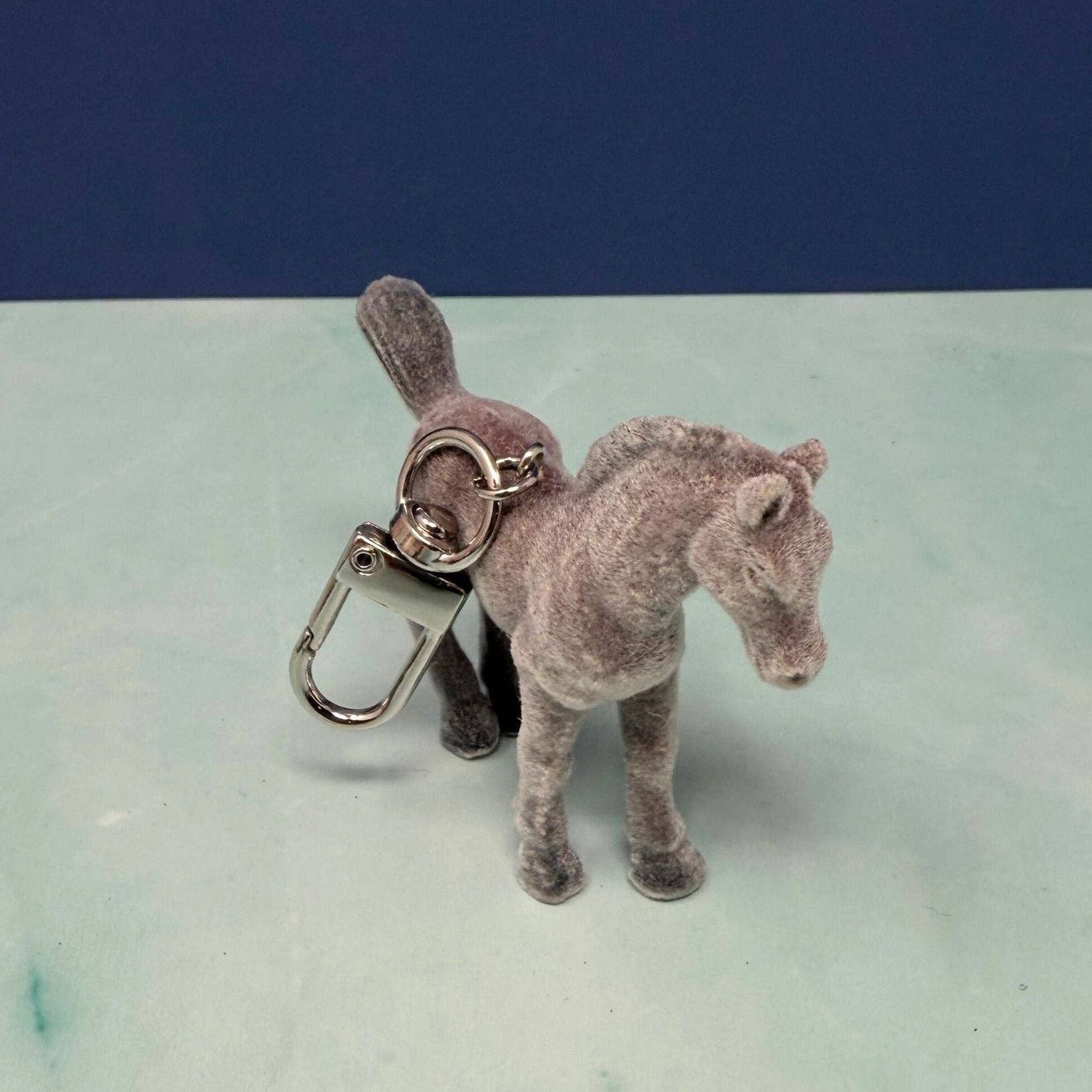 Plush horse keychain on a light green surface with a blue background