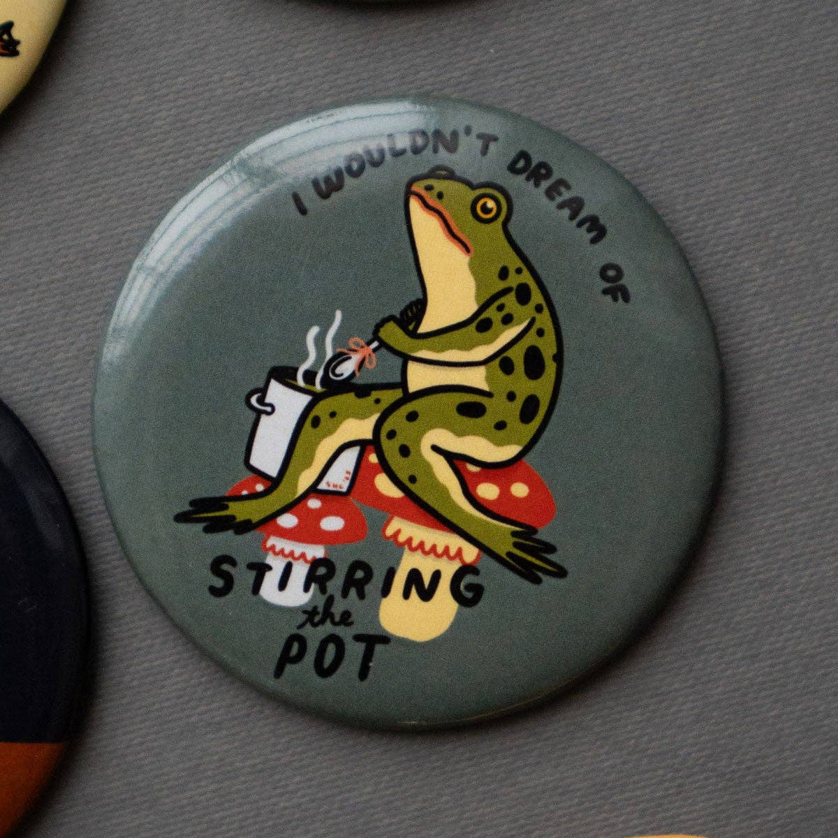 Button badge with a frog illustration and text on a gray background