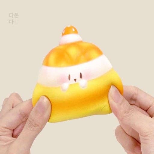 Squishy toy shaped like a cartoon character with a colorful design held by hands against a beige background.