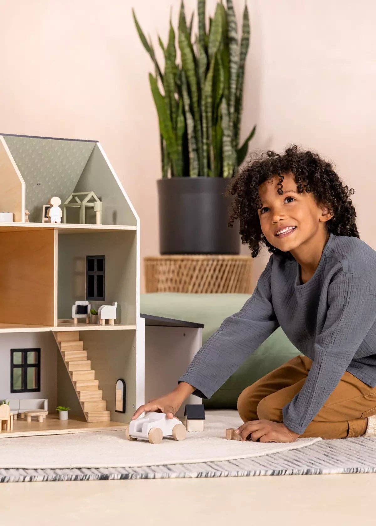 Child playing with a toy car in a room with a dollhouse and plant.
