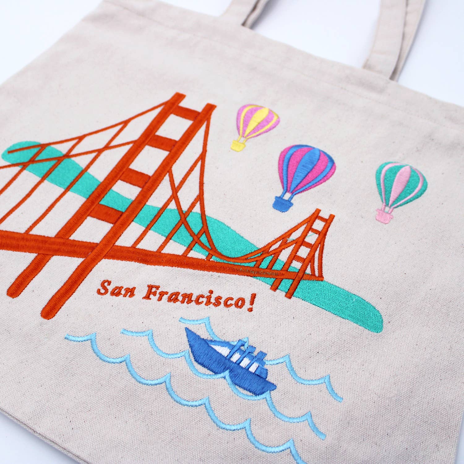 Tote bag with embroidered design of the Golden Gate Bridge, hot air balloons, and a ship, featuring the text 'San Francisco!'.
