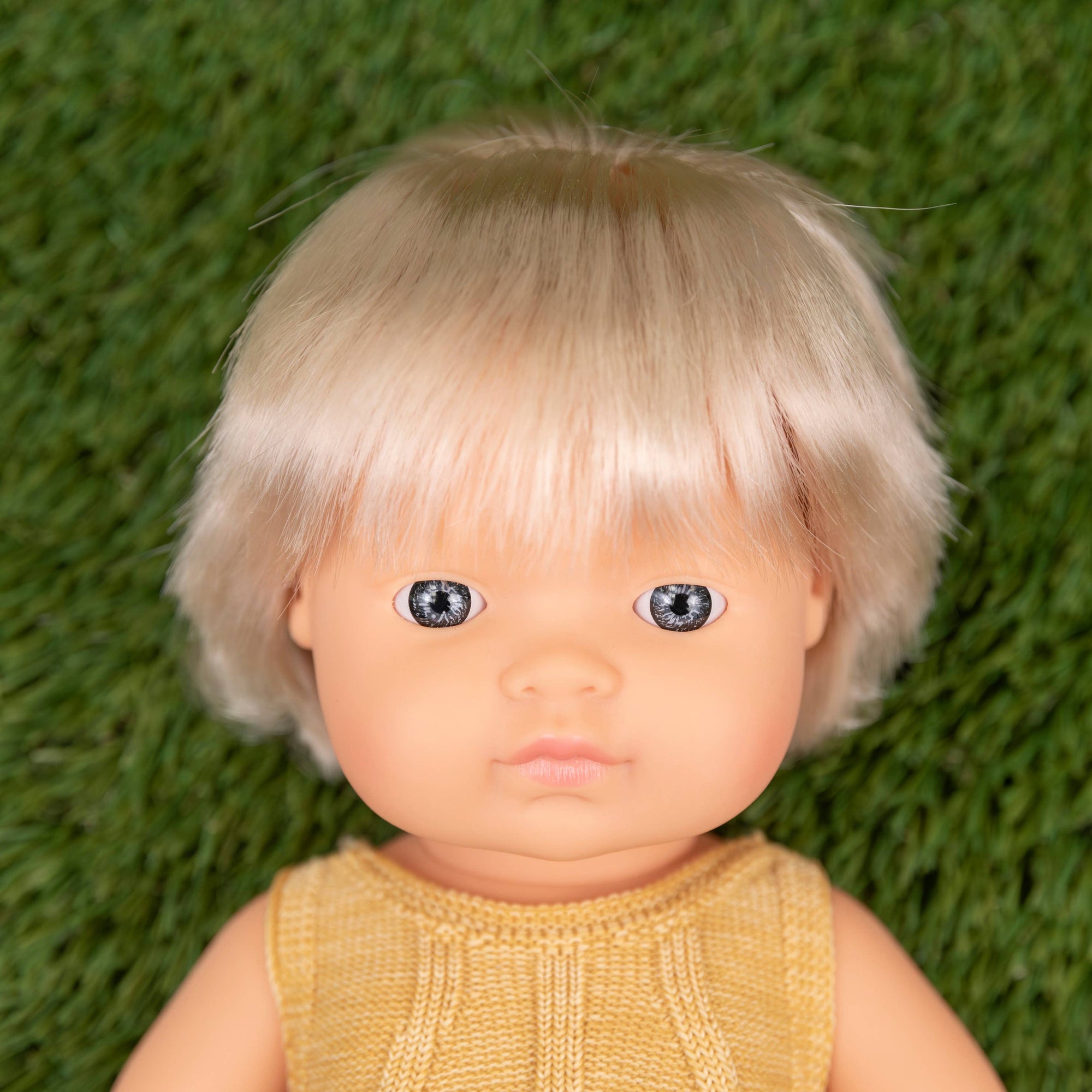 Toy doll with blonde hair and a yellow dress on a green textured background