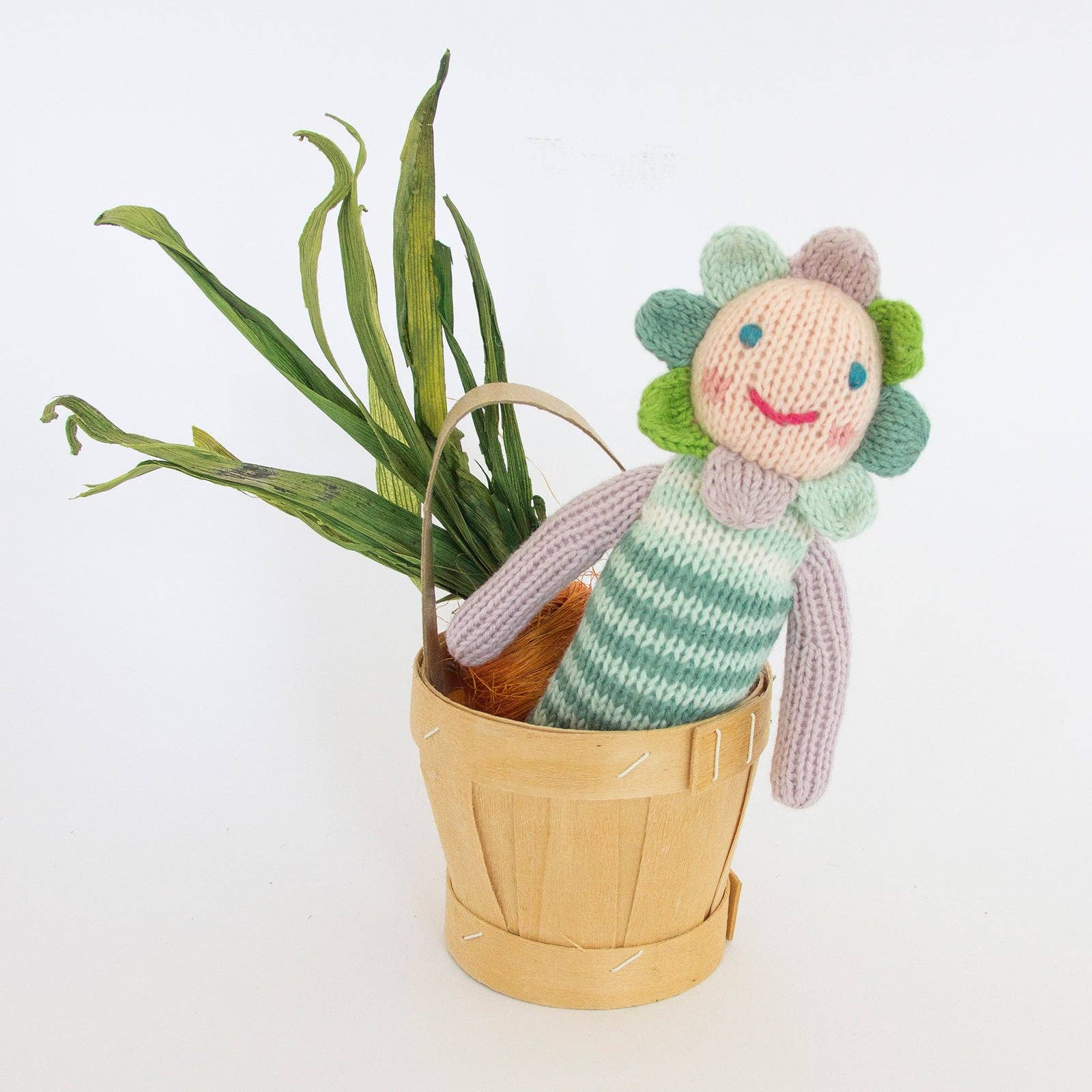 Knitted flower-shaped toy with striped body in a wooden basket on a white background