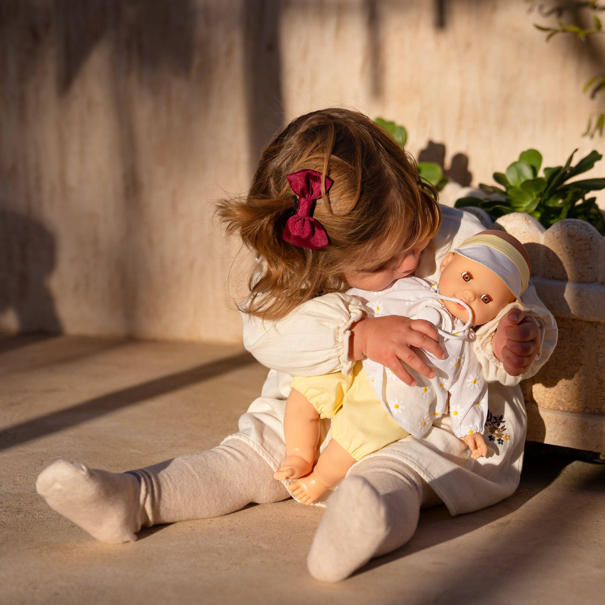 Child holding a baby doll in a sunlit outdoor setting