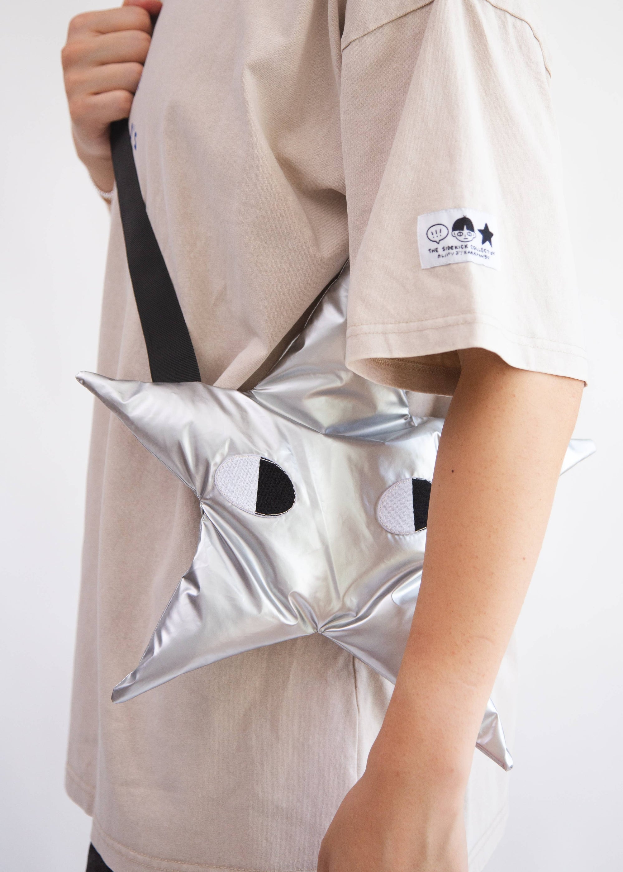 Person holding a silver star-shaped bag with black accents on a plain background