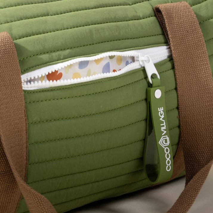 Green quilted bag with brown strap and floral pocket with zipper pull on a light gray background