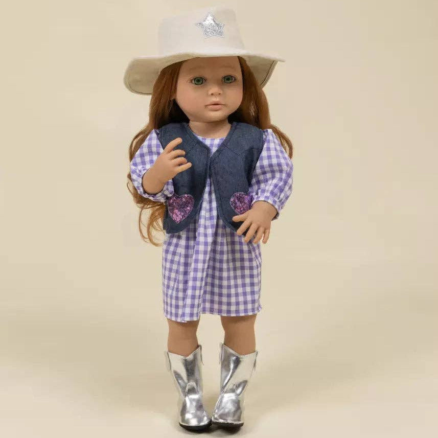 A doll with long brown hair wearing a white cowboy hat, a purple and white gingham dress, a navy vest with purple heart patches, and shiny silver cowboy boots, standing against a plain beige background.