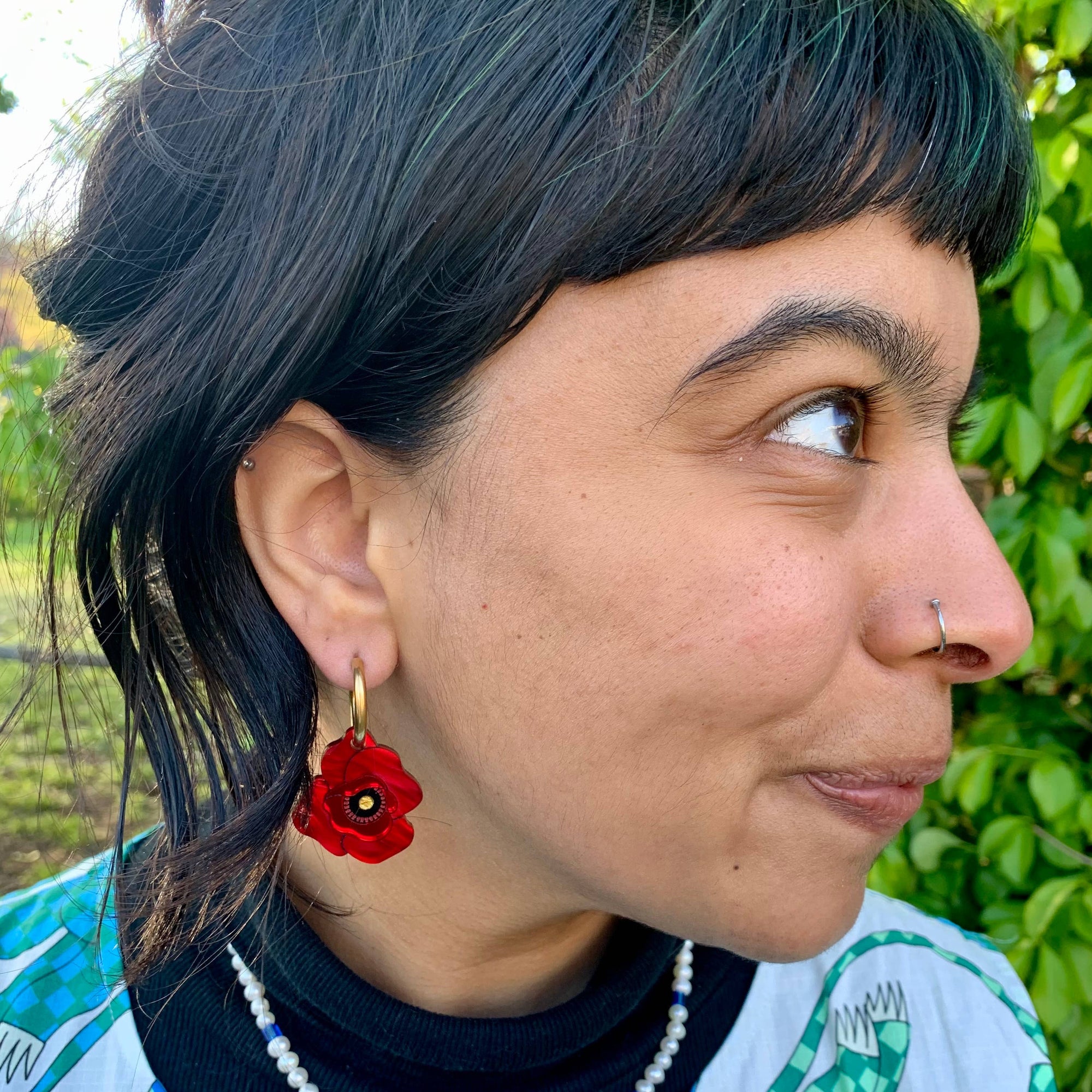 Person wearing a colorful shirt with a red flower earring outdoors