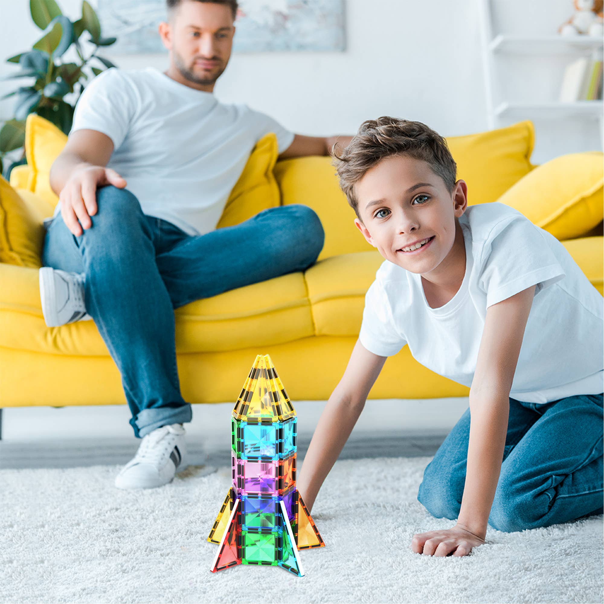 Child playing with a colorful toy rocket on the floor, with an adult sitting on a yellow couch in the background.