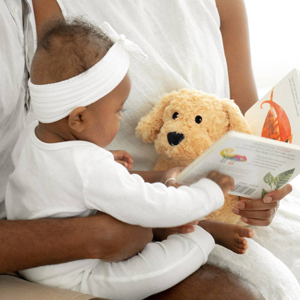 Baby holding a teddy bear and a book with an adult sitting next to them
