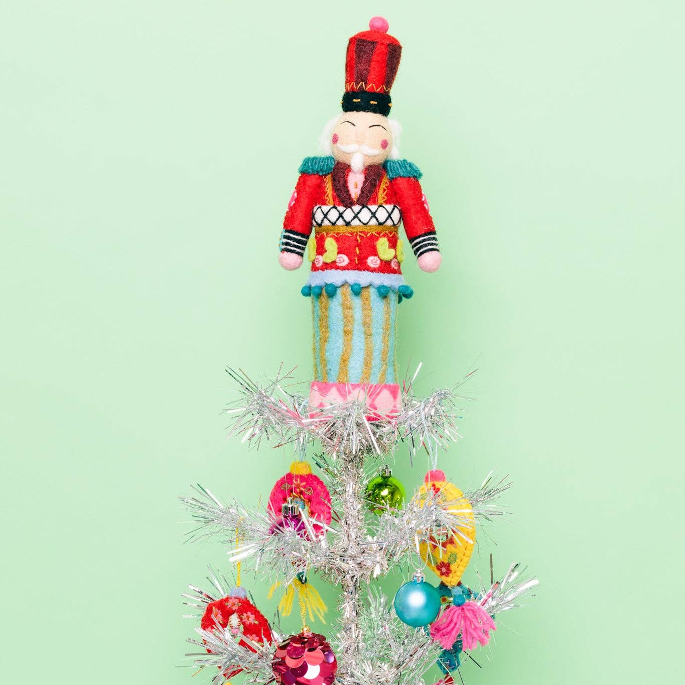 Decorative Christmas tree with colorful ornaments and a nutcracker figure on a light green background
