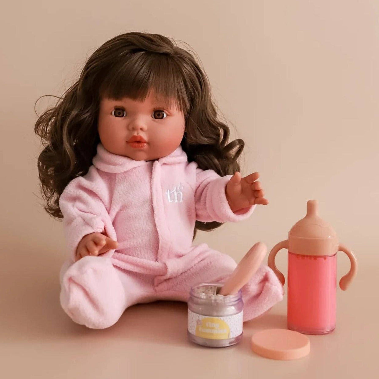 Doll in a pink outfit with a bottle and jar on a beige background